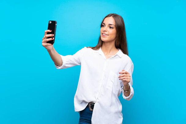 Jovem mulher sobre isolado fundo azul fazendo uma selfie - Foto, Imagem