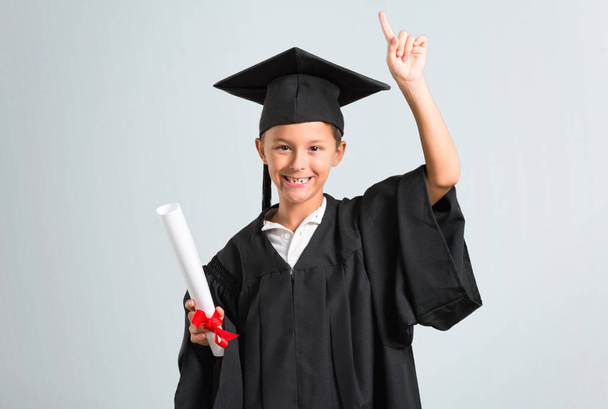 Little boy graduating standing and thinking an idea on grey background - Foto, Imagen