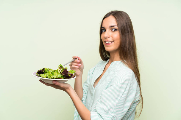 Mujer joven con ensalada sobre pared verde aislada
 - Foto, imagen