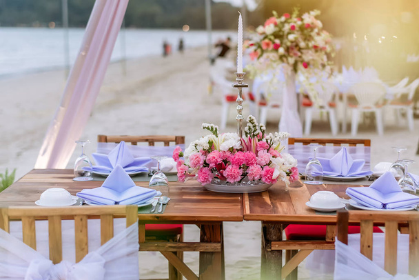 Romanttinen ruokapöytä rannalla. Pöydän kattaminen luksushäissä ja Kauniita kukkia pöydällä. päivällispöytä hiekkarannalla
. - Valokuva, kuva