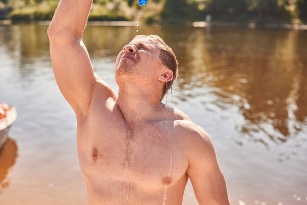 lihaksikas mies, jolla on alaston vartalo, seisoo joen tai järven rannalla kuumana päivänä ja juo kylmää vettä
 - Valokuva, kuva