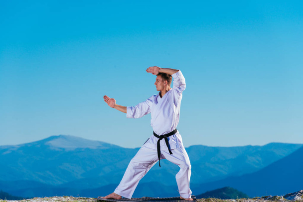 Blond karate atleta robi kata na szczycie góry podczas wykonywania szereg kopnięć, ciosów i bloków na szczycie góry w słoneczny dzień. - Zdjęcie, obraz