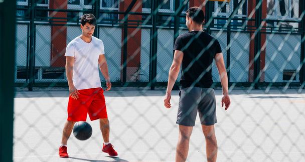 Deux joueurs de basket-ball forts jouant au ballon sur un terrain de basket urbain, tout en portant une tenue noire et rouge
. - Photo, image
