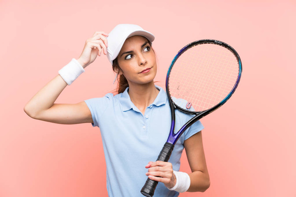 疑いを持ち、混乱した顔の表情を持つ孤立したピンクの壁の上に若いテニス選手の女性 - 写真・画像