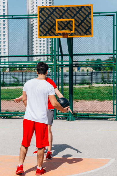 白い高層ビルが青空に近づく中、都会のバスケットボール場でボール(プッシュ、ドリブル)をするバスケットボール選手. - 写真・画像