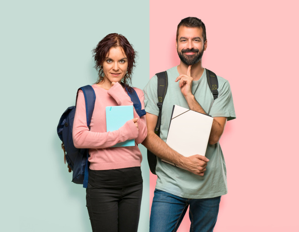Deux étudiants avec des sacs à dos et des livres souriants et regardant vers l'avant avec un visage confiant sur un mur coloré
 - Photo, image