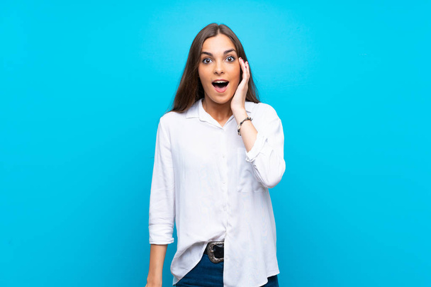 jonge vrouw over geïsoleerde blauwe achtergrond met verrassing en geschokt gezichtsuitdrukking - Foto, afbeelding