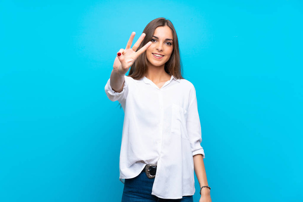 junge Frau vor isoliertem blauem Hintergrund glücklich und zählt mit den Fingern drei - Foto, Bild