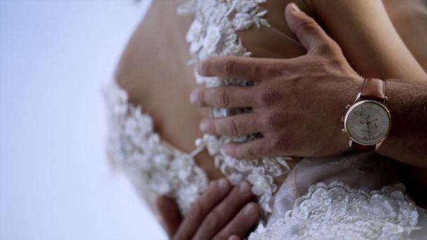 妻を抱きしめる夫のクローズアップ。アクション。夫は白いウェディングドレスで妻のウエストに優しく触れます。結婚式のコンセプト - 写真・画像
