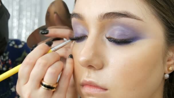 Young beautiful sexy girl models make blue evening make up smoky eyes and with false eyelashes. Eyes with multi-colored contact lenses - Footage, Video