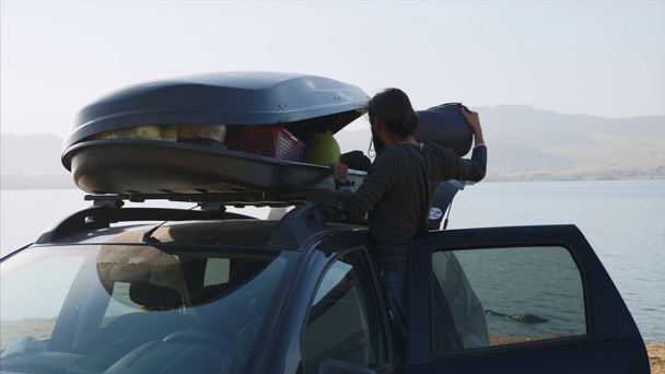 Jovem barbudo tirando um equipamento de acampamento da caixa do telhado do carro
 - Filmagem, Vídeo