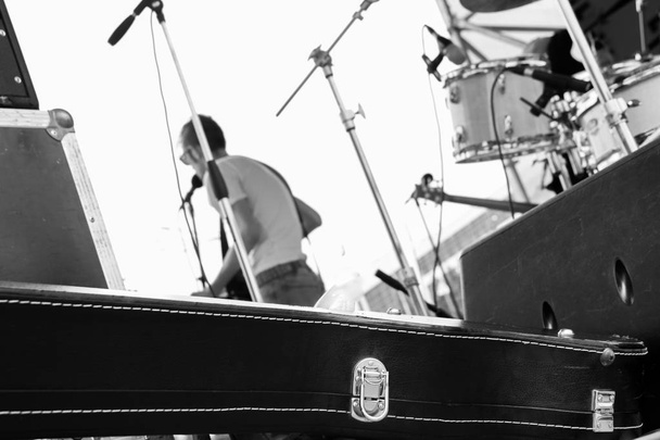 Το μουσικό συγκρότημα παίζει σε υπαίθριο φεστιβάλ, θέα από πίσω από τη σκηνή, μαύρη θήκη για κιθάρα, τραγουδίστρια στη σκηνή, μαύρη και λευκή φωτογραφία - Φωτογραφία, εικόνα