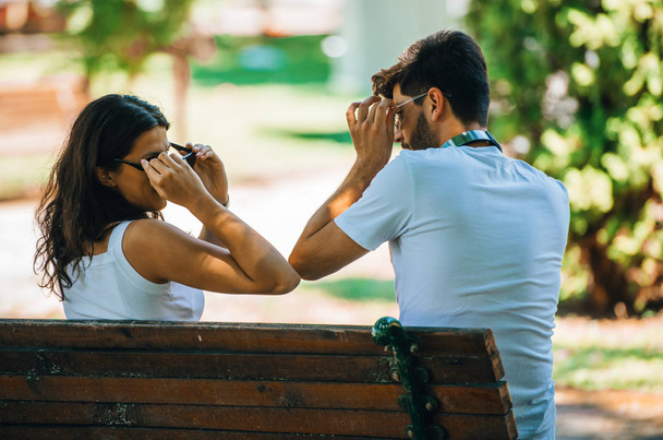 Bir çift genç aşık parktaki ahşap bankta oturuyor. - Fotoğraf, Görsel