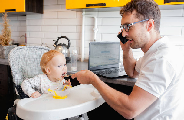 Happy young father working at home and sitting with a baby girl. - Фото, изображение