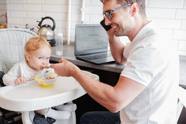 Ευτυχισμένο νεαρό πατέρα που εργάζεται στο σπίτι και κάθεται με ένα μωρό κορίτσι. - Φωτογραφία, εικόνα
