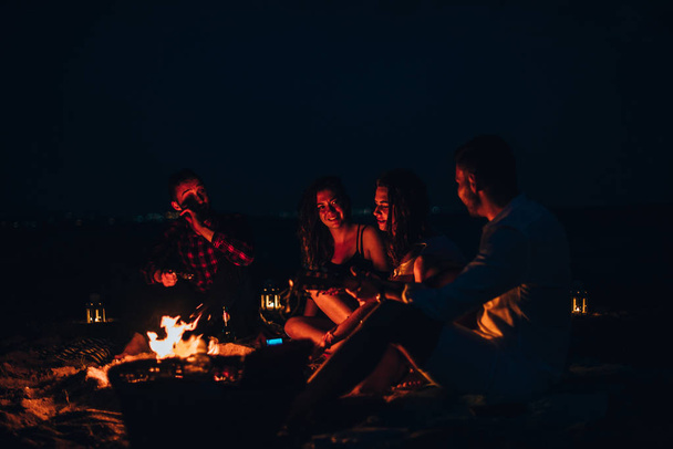 Gruppo di amici in festa sulla spiaggia seduti intorno al fuoco - Foto, immagini