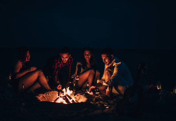 Przyjaciele cieszą się muzyką w pobliżu ogniska w nocy na piaszczystej plaży - Zdjęcie, obraz