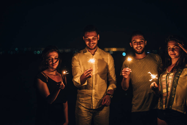 Группа друзей зажигает огненные палки в темноте и en - Фото, изображение