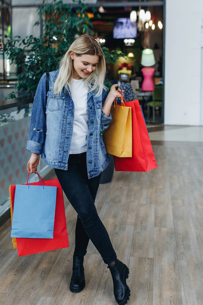 Mode einkaufen junge Frau Porträt. Schönheit Frau in einer Jeansjacke mit Einkaufstaschen in einem Einkaufszentrum stehen. Shopper, Verkauf, Einkaufszentrum - Foto, Bild