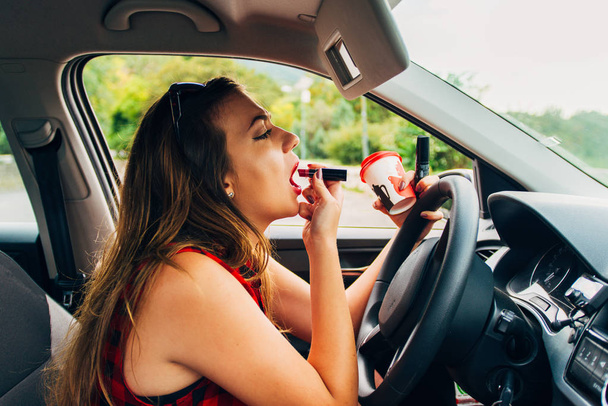 Muito jovem mulher imprudente está em seu carro segurando café e fixação de seu batom - Foto, Imagem