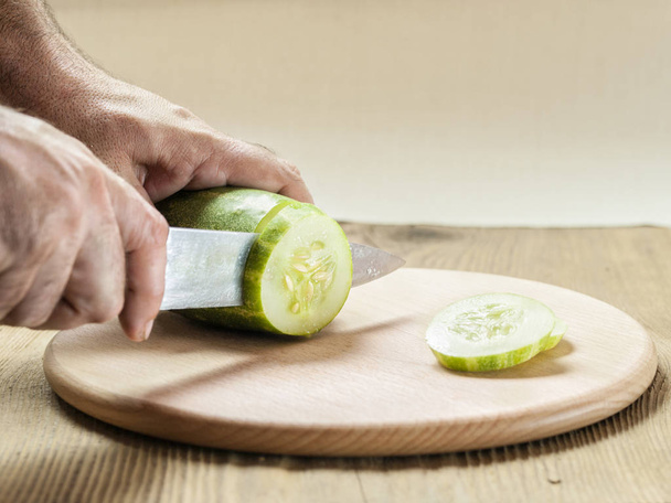 Las manos de los hombres cortan un pepino verde en rodajas con un cuchillo
 - Foto, Imagen