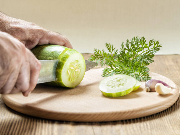 Männerhände schneiden eine grüne Gurke mit einem Messer in Scheiben - Foto, Bild