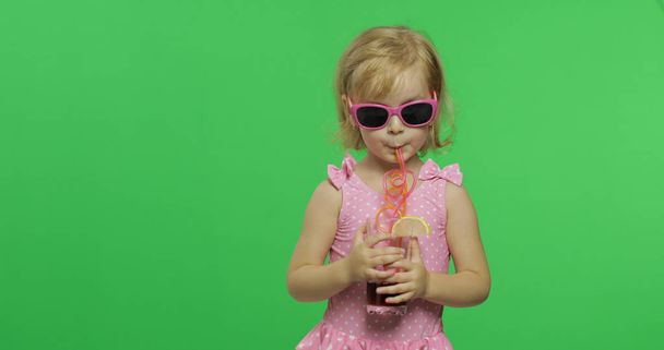 Bambino in costume da bagno rosa beve succo di cocktail con paglia da bere. Chiave cromatica
 - Foto, immagini