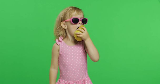 Child in pink swimsuit and sunglasses eats a green pear. Chroma Key - Photo, image
