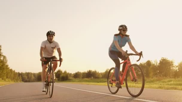 Egy férfi és egy nő lovagolni sport kerékpárok az autópályán napnyugtakor a sebességváltó és védősisakok lassítva 120 fps - Felvétel, videó
