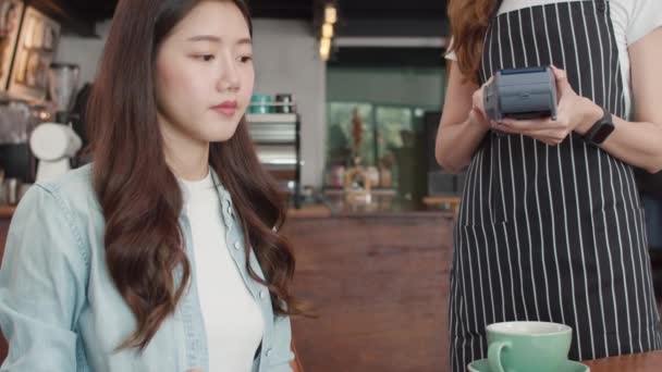 Young Asian freelance women pay contactless credit card at coffee shop. Asian happy girl barista waiter wear gray apon holding credit card reader machine for customer can pay with technology in cafe. - Footage, Video