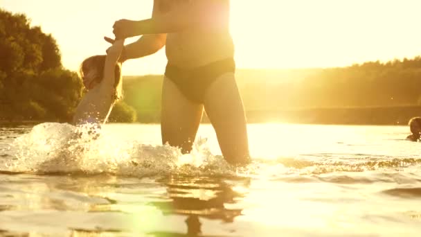 Buon papà e gioioso bambino sorridente, fare il bagno e giocare in acqua al tramonto dorato. padre e figlioletta stanno giocando in acqua sulla spiaggia al sole caldo
. - Filmati, video