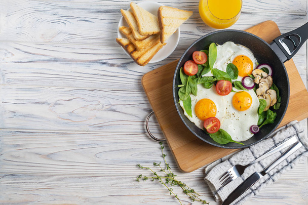 Жареные яйца с помидорами, грибами и листьями шпината на сковородке
 - Фото, изображение