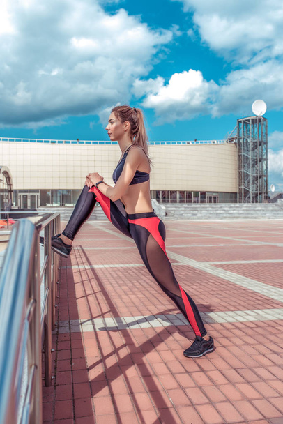 beautiful woman does stretching the muscles of her legs, before jogging in the city, the athlete is fitness in the summer in the city. Sportswear Leggings Top. - Фото, зображення