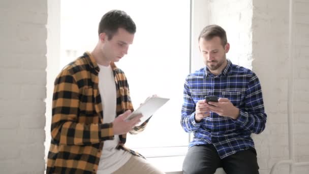 Νέοι άνθρωποι απασχολημένοι με τη χρήση ψηφιακών συσκευών ενώ κάθονται στο παράθυρο - Πλάνα, βίντεο