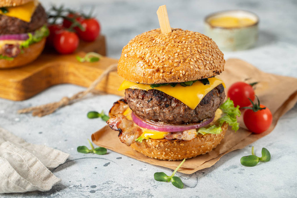 eine Reihe hausgemachter köstlicher Burger aus Rindfleisch, Speck, Käse, Salat und Tomaten auf hellem Betongrund. Fett und ungesunde Lebensmittel aus nächster Nähe - Foto, Bild