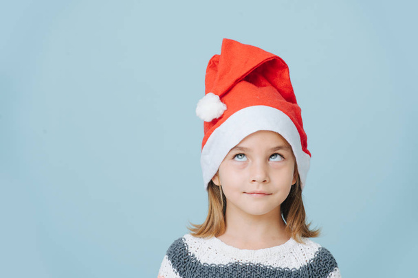 Portrait of cute little first grader girl in a santa's hat and knitted sweater. - Фото, зображення