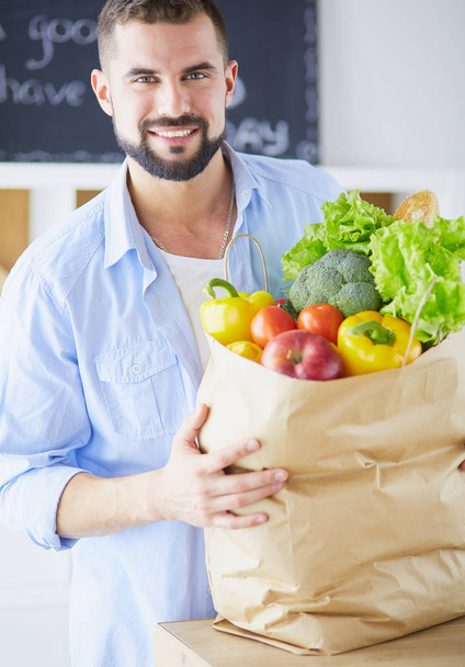 Man holding paper bag full of groceries on the kitchen background. Shopping and healthy food concept - Foto, imagen