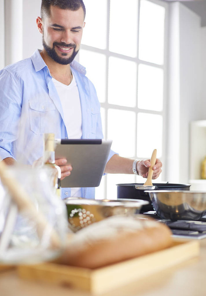 Man following recipe on digital tablet and cooking tasty and healthy food in kitchen at home - Fotoğraf, Görsel