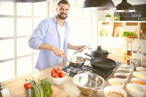 Man following recipe on digital tablet και το μαγείρεμα νόστιμο και υγιεινό φαγητό στην κουζίνα στο σπίτι - Φωτογραφία, εικόνα