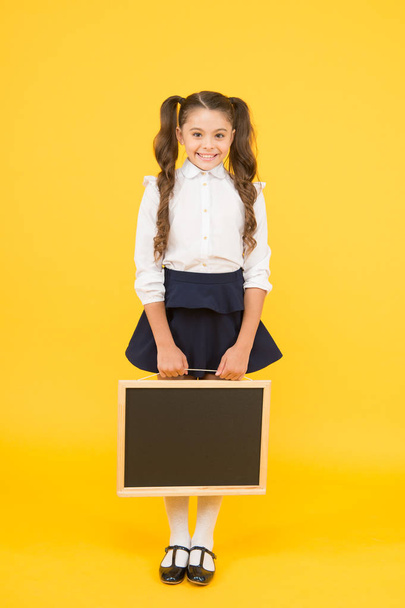 Preparing small child for school. Small girl holding black-board on yellow background. Small kid with empty chalkboard for your text. Small schoolchild holding blackboard for advertising, copy space - Foto, Bild