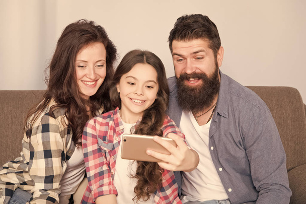 家庭での幸せな家族。少女は、母親と父親と一緒にスマート フォンを使用します。ハッピーな気分の家族。幸せな家族の selfie。ひげを生やした男性と女性の娘子。幸せな家族。明るい瞬間をキャプチャ - 写真・画像