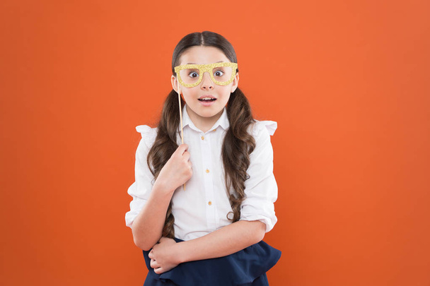 School party concept. What does it mean being smart. Little smart schoolgirl on orange background. Child smart look through photo booth props eyeglasses. Small kid wearing eye glasses in smart style - Photo, image