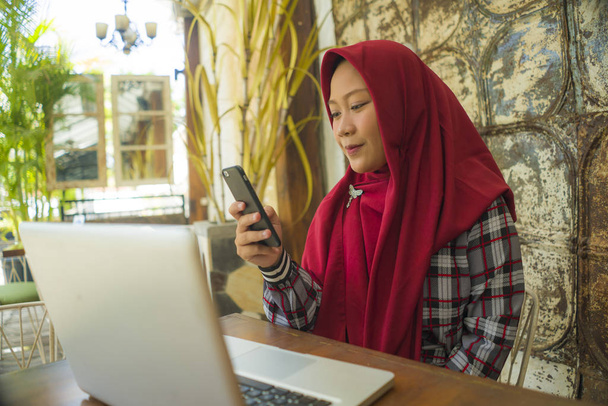Muslim student girl in hijab networking with laptop . Young happy and beautiful Asian Indonesian woman in Islam head scarf working at cafe using computer and mobile phone - Фото, зображення
