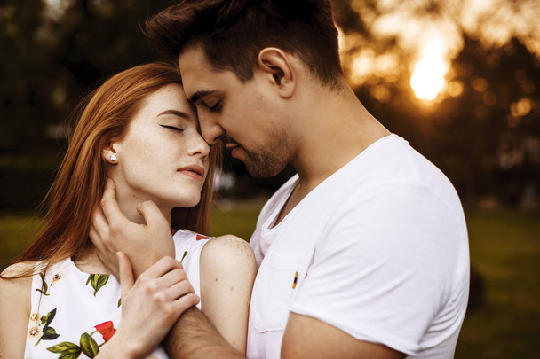 Retrato vista lateral de una encantadora pareja caucásica abrazándose antes de besarse contra el atardecer con los ojos cerrados afuera
. - Foto, imagen