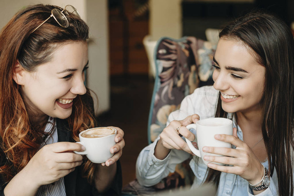 Две красивые женщины пьют кофе и смеются, рассказывая сказки.
 - Фото, изображение