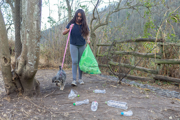 Ένα κορίτσι με το σκύλο της συλλέγει πλαστικά μπουκάλια στη μέση του - Φωτογραφία, εικόνα