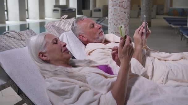 Ευτυχισμένο ηλικιωμένο ζευγάρι χρησιμοποιώντας τα τηλέφωνα χαλαρωτικό στο ξενοδοχείο - Πλάνα, βίντεο