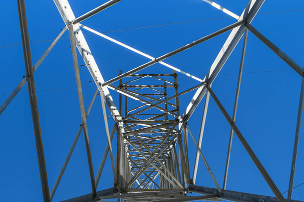 Supports high-voltage power lines against the blue sky. View from the bottom up - Zdjęcie, obraz