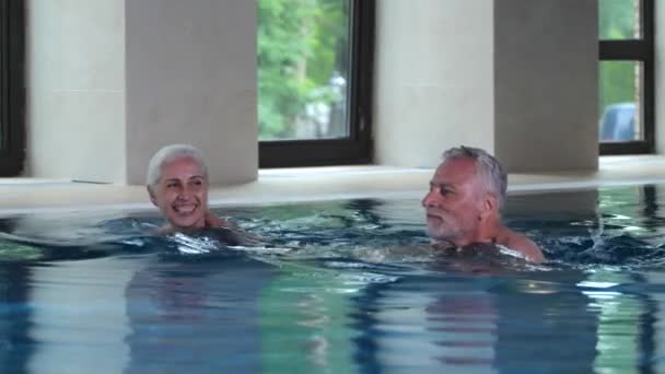 Happy elderly couple swimming in indoor hotel pool - Footage, Video