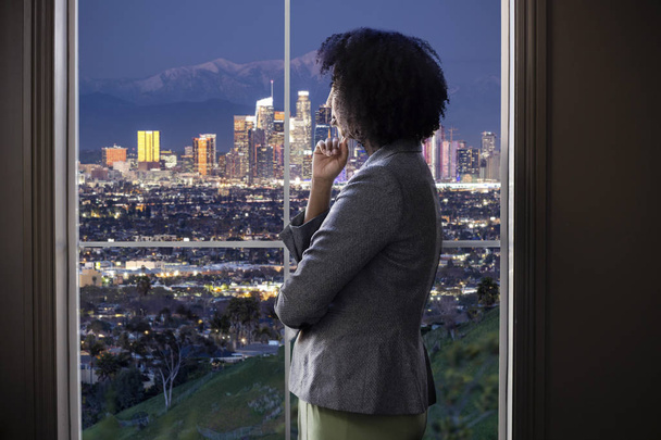 Czarna kobieta biznesu patrząc na okno biura w Los Angeles. Wygląda jak kobieta architekt myślenia rozwoju miejskiego lub Burmistrz miasta lub gubernator planowania zagospodarowania przestrzennego prawa.  - Zdjęcie, obraz